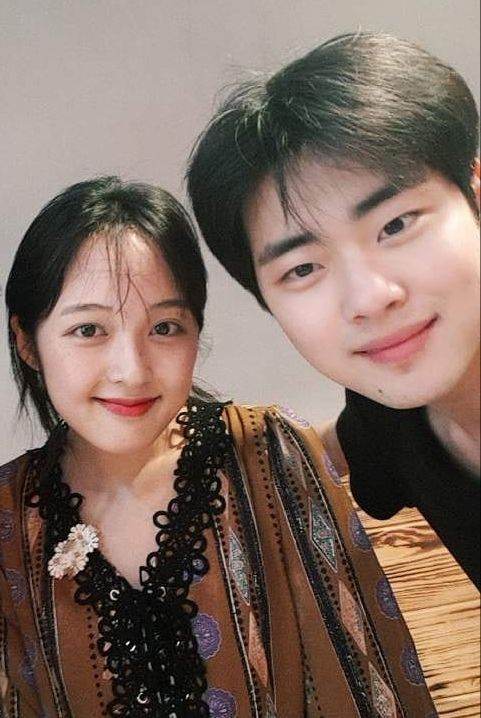 兩位穿著印花服裝的人親密地站在一起，其中一人佩戴花飾品。