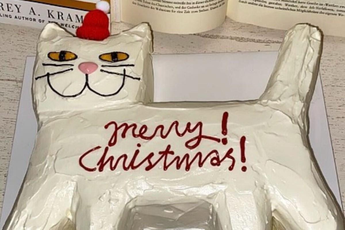 クリスマス風にデザインされた白い猫の形のケーキには、赤いサンタ帽と『merry Christmas!』と書かれている。背景には布製のテーブルマットが置かれている。