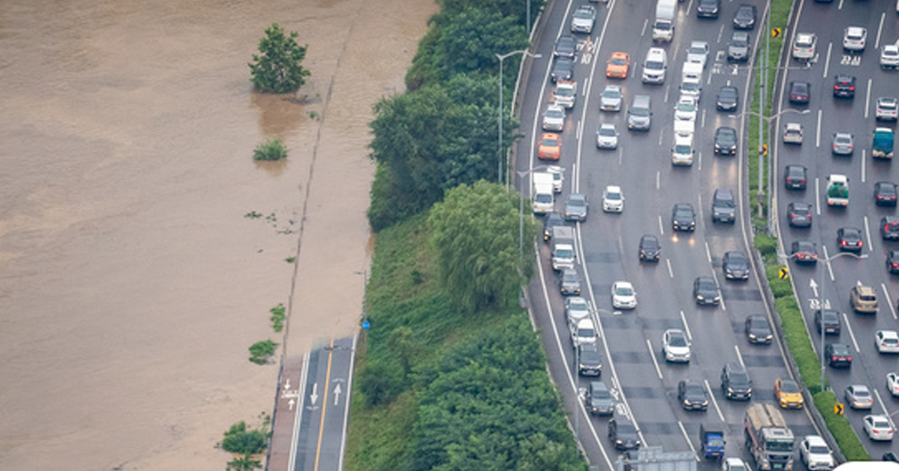 高空視角下，洪水泛濫淹沒道路，旁邊汽車車流緩慢進行