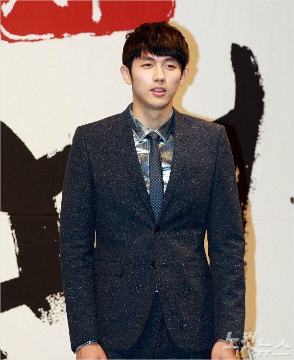 身穿藍色西裝搭配銀色襯衫和藍色領帶的男性，背景為日本風格的海報