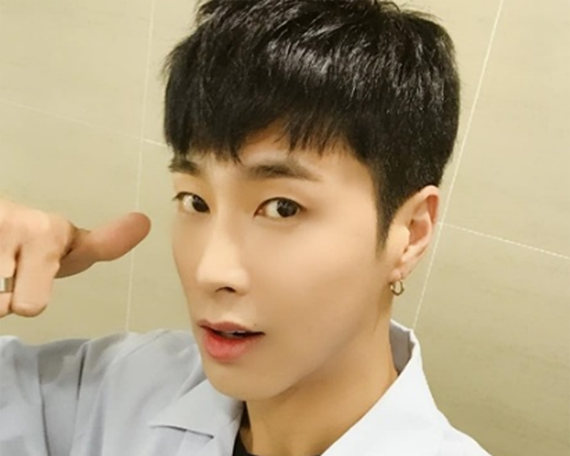 允浩穿著白色上衣，雙手比出讚的手勢，並微笑地面對鏡頭。