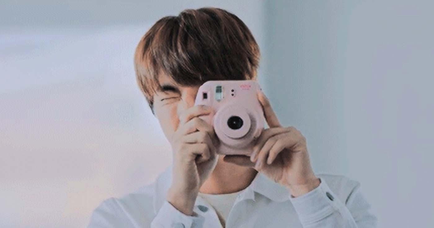 ชายหนุ่มชาวเกาหลีถือกล้องถ่ายรูปในขณะที่เขาอยู่ในบรรยากาศที่เต็มไปด้วยแสงธรรมชาติ เหมาะสำหรับการถ่ายภาพแบบแฟนหนุ่มสไตล์เกาหลี