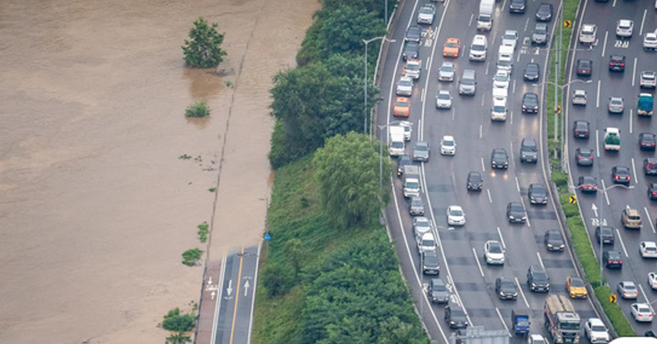 韓國漢江水位上漲導致河岸淹水，旁邊的主要道路上車輛擁堵，顯示交通受到影響。