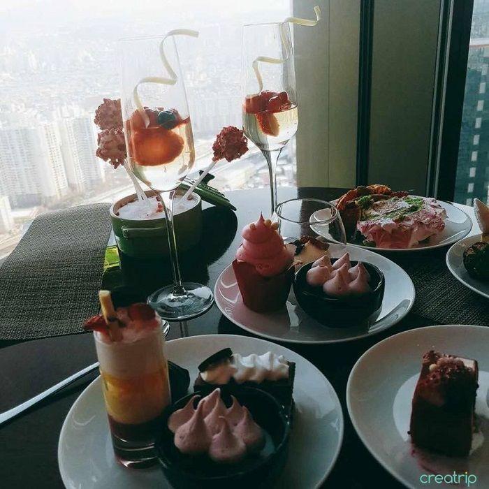 靠窗座位上的下午茶展示，桌上的甜點和酒杯以及窗外的城市景觀交相輝映，讓人放鬆愉快。