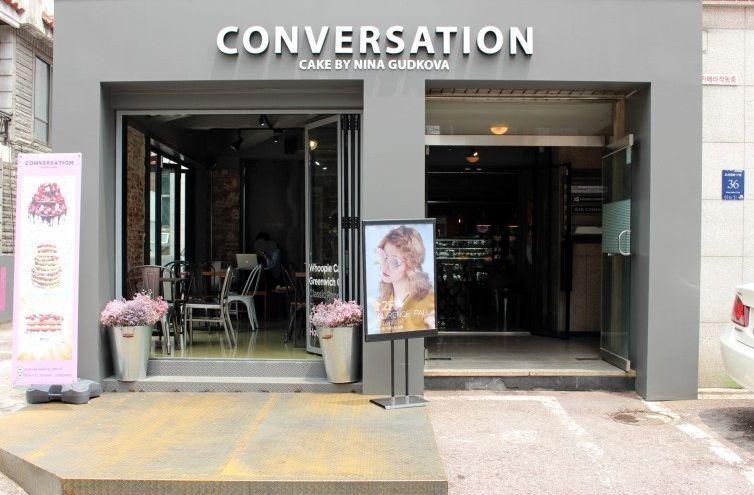 CONVERSATION咖啡館的外立面，霓虹燈下映照出時尚與都市風格，內部可見白色裝飾設計。