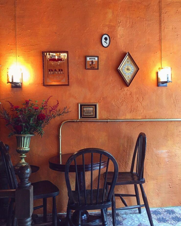 Louloudi咖啡廳內的個性化裝飾牆，橙色的牆壁上掛著幾幅畫，旁邊擺放著一束鮮花，營造溫馨環境。