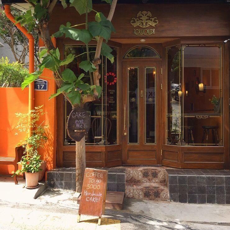 Louloudi咖啡館的外觀，裝飾著木質門面和玻璃窗，咖啡館招牌上寫有"咖啡和自製蛋糕".