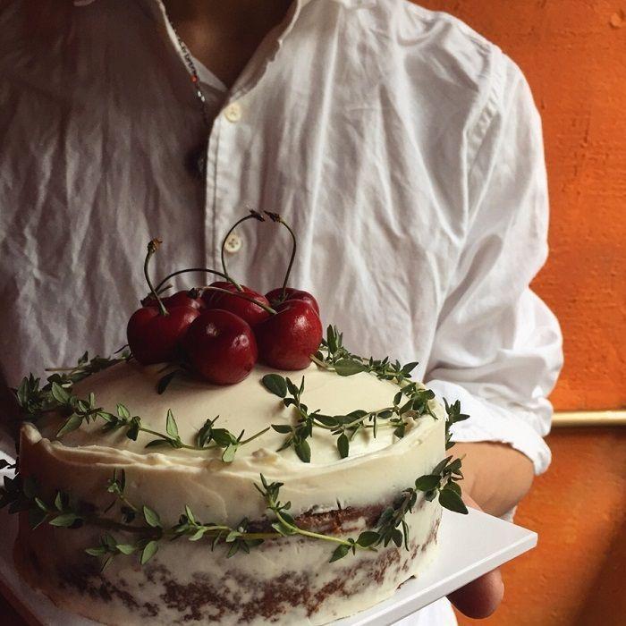 一款用鮮花和新鮮水果裝飾的蛋糕，蛋糕頂部有一圈新鮮的紅色櫻桃，蛋糕展示在白色背景的襯托下。