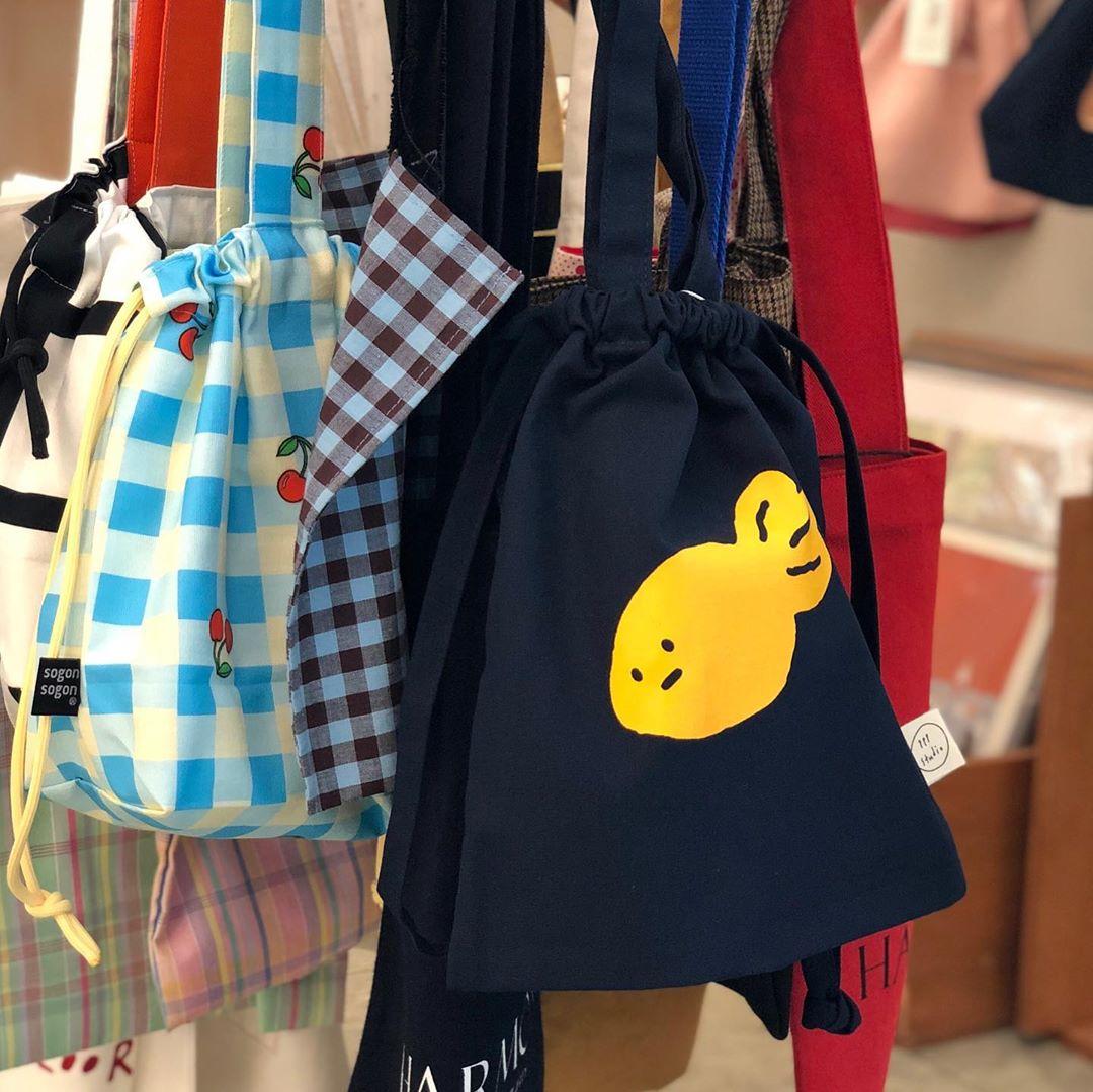 韓国雑貨店の店内ディスプレイにサンプルとして並べられたカラフルなバッグシリーズ。チェック柄やシンプルなデザインのトートバッグ。