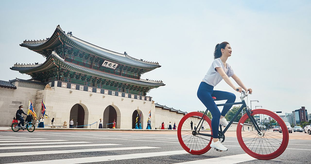 韓國首爾的光化門前，一位女士正在騎自行車，背景是傳統的韓國建築。