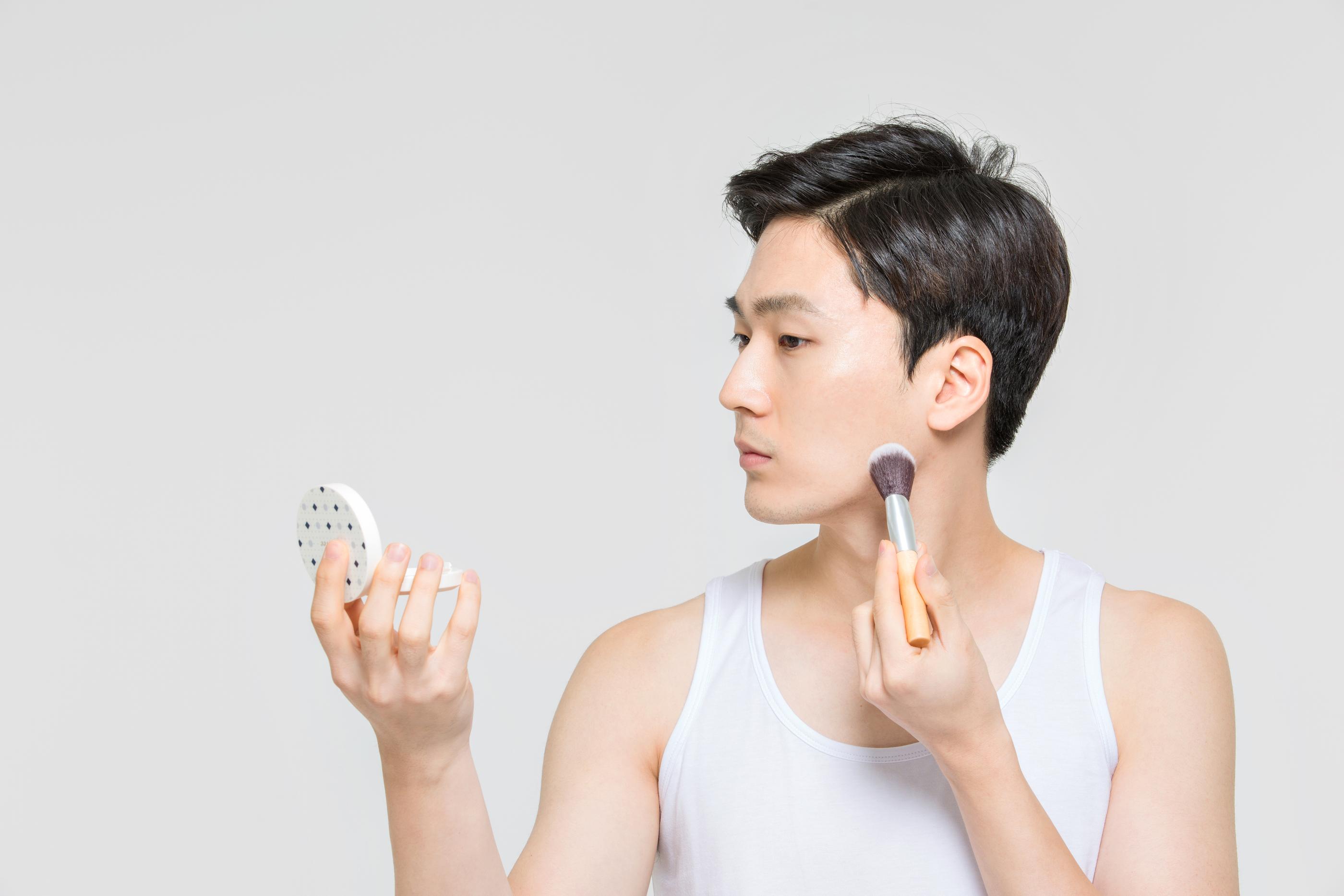 Người đàn ông Hàn Quốc đang trang điểm với dụng cụ trang điểm và gương cầm tay