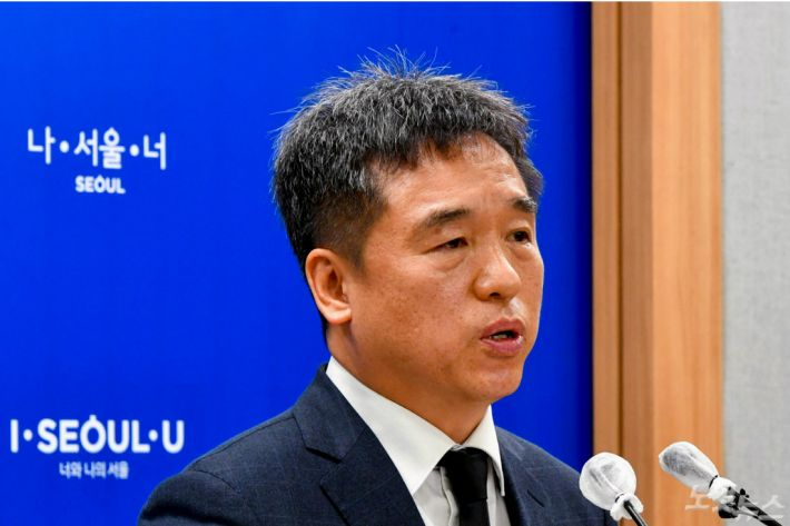 首爾市政府發言人正在新聞發布會上發表聲明，背景顯示首爾市的標誌