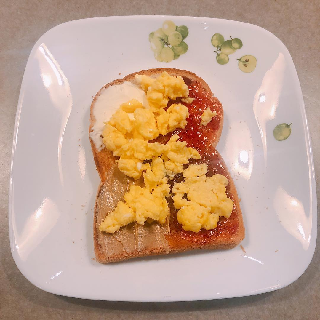 一块吐司上涂有花生酱和草莓果酱，上面覆盖有充分煎炒的鸡蛋，呈现金黄色诱人的光泽。这道早餐组合提供了丰富的甜味和滑润的质感。