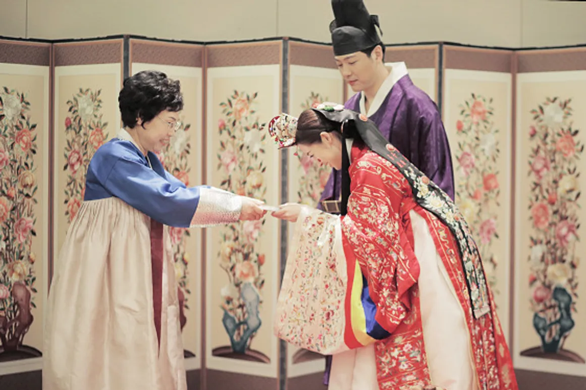 传统韩式婚礼仪式场景：一对穿着传统韩服的新人在长辈面前进行婚礼仪式，展示了韩国传统文化。