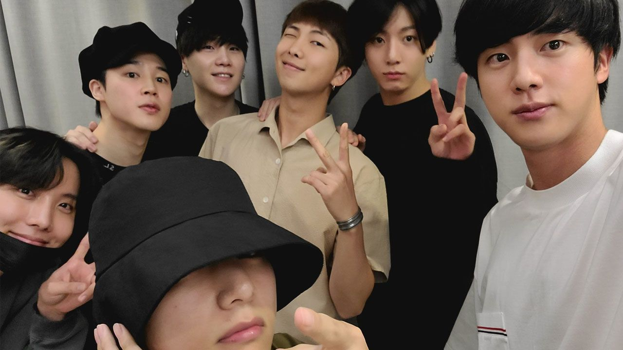 ภาพถ่ายกลุ่มของสมาชิก BTS ยืนถ่ายภาพในชุดลำลองพร้อมแสดงสัญลักษณ์ V-sign
