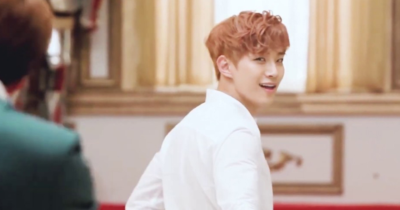 一名穿著白襯衫的韓國男子往前走，琥珀色的光線從窗外照進房間。