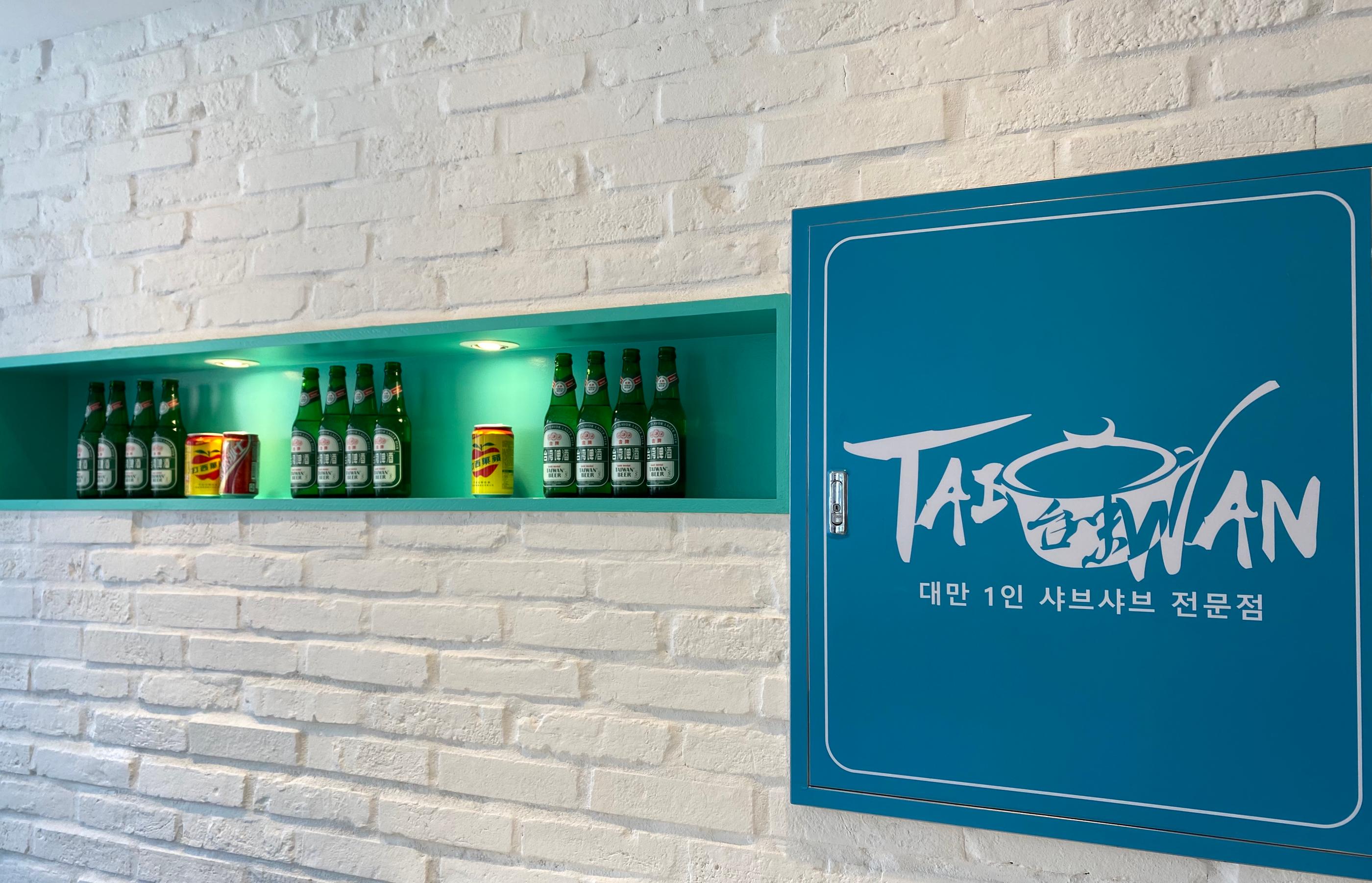 臺灣火鍋專賣店的內部裝潢，展示了幾瓶臺灣啤酒與飲料罐，綠色牆面裝飾。