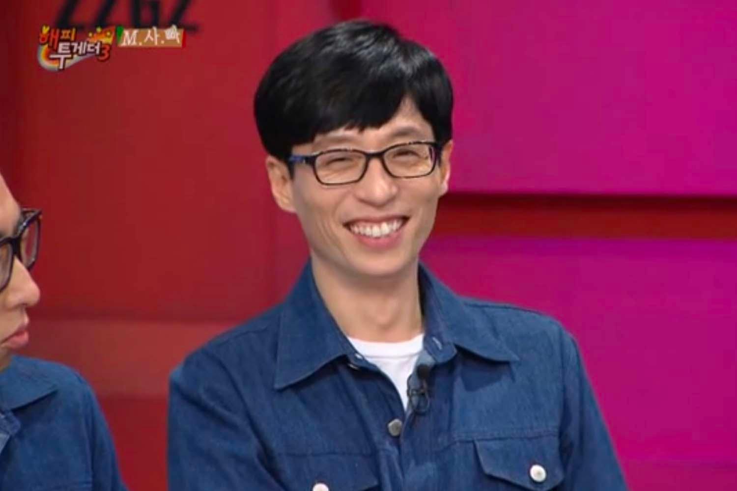 ยูแจซอกสวมเสื้อแจ็คเก็ตยีนส์กำลังนั่งในรายการโทรทัศน์เกาหลีบนพื้นหลังสีชมพูสดใส