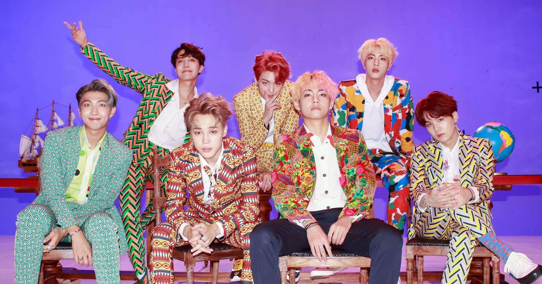 防彈少年團（BTS）身著色彩鮮豔的西裝坐在紫色背景前，展現出時尚及創意的氣氛