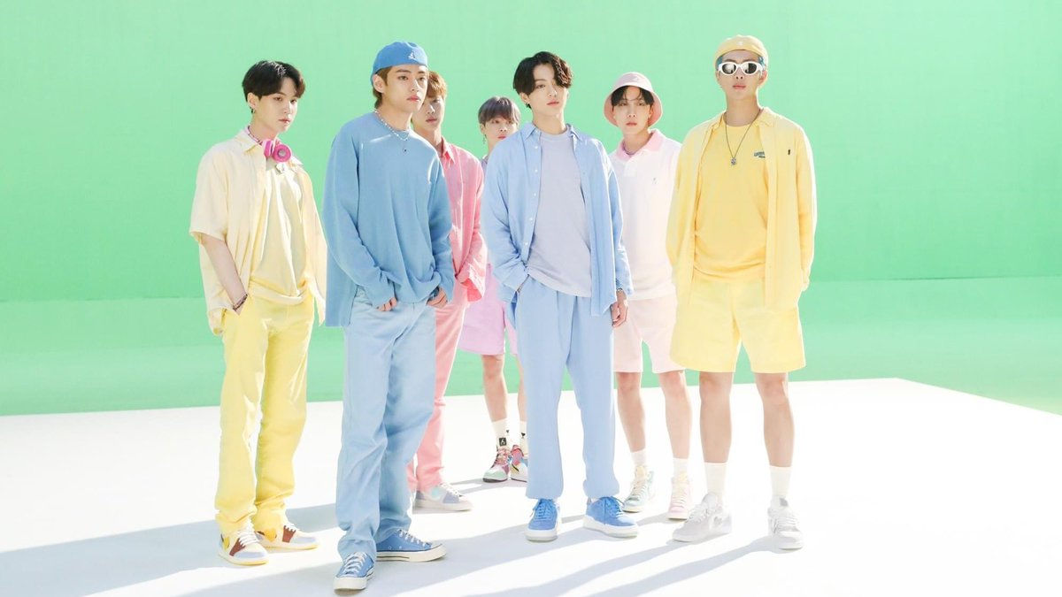 防彈少年團（BTS）穿著粉色及白色的時尚服裝，背景是綠色的拍攝場地，展現出充滿活力的氛圍