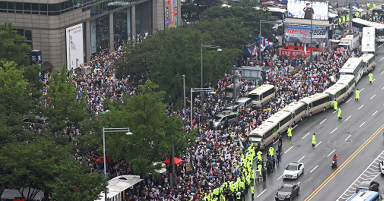 ภาพมวลชนในการชุมนุมในเมืองเกาหลีใต้ มีตำรวจและรถบัสตำรวจอยู่ใกล้