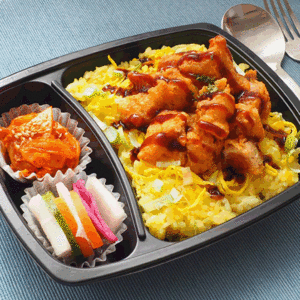 便利商店便當展示圖片，盒飯包括雞肉、泡菜、以及色彩鮮艷的韓式小菜，擺放在藍色桌布上。