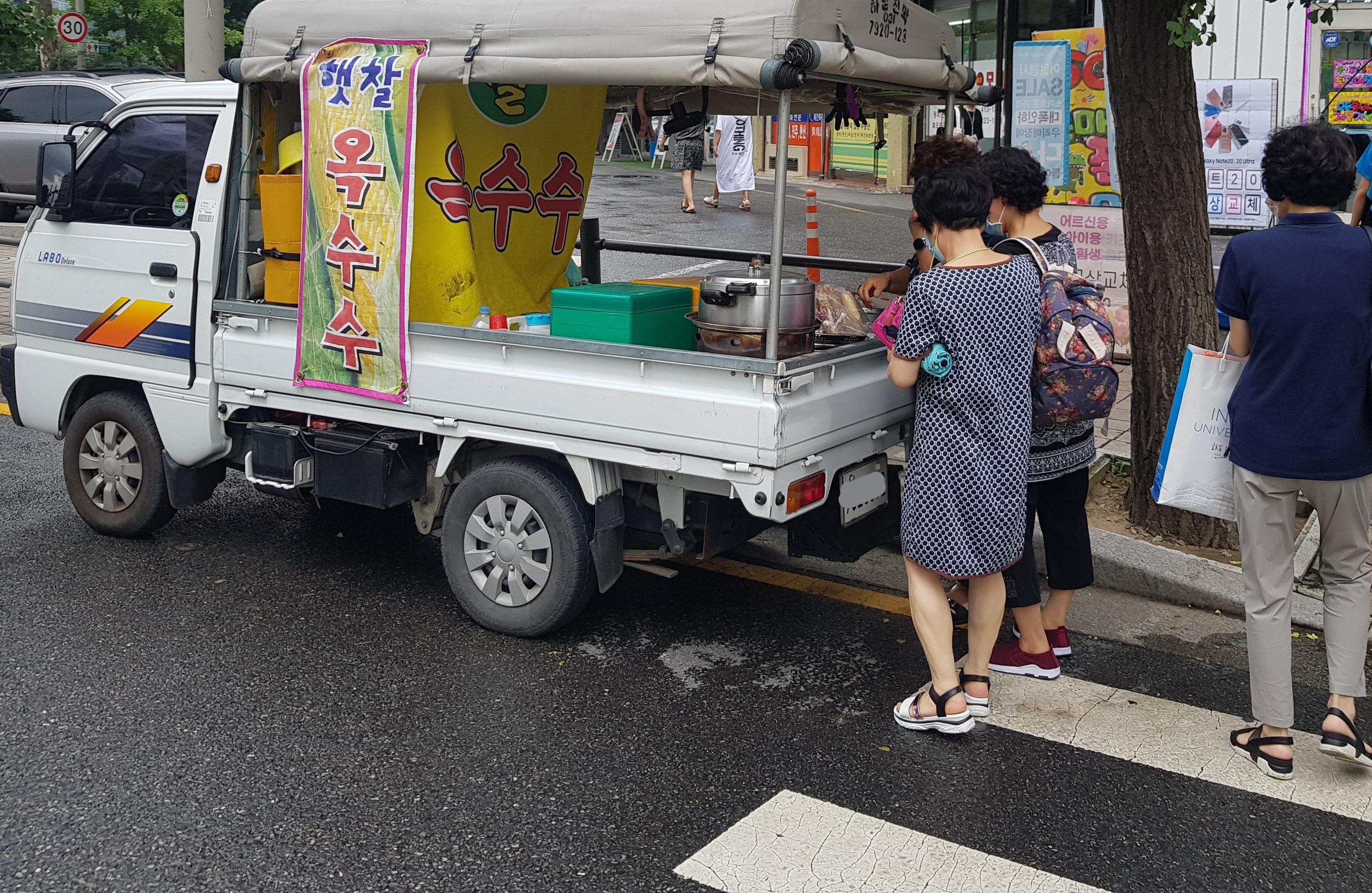 道端で販売されている韓国のトウモロコシ、옥수수 オクスス、蒸し器を積んだトラックと買い物をする人々の姿。