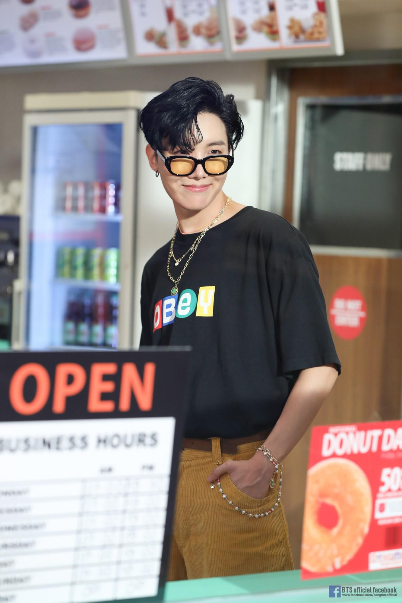 BTS 的成員站在店鋪櫃台前,穿著印有 OBEY 字樣的黑色T恤,背景是商店選單和商品展示