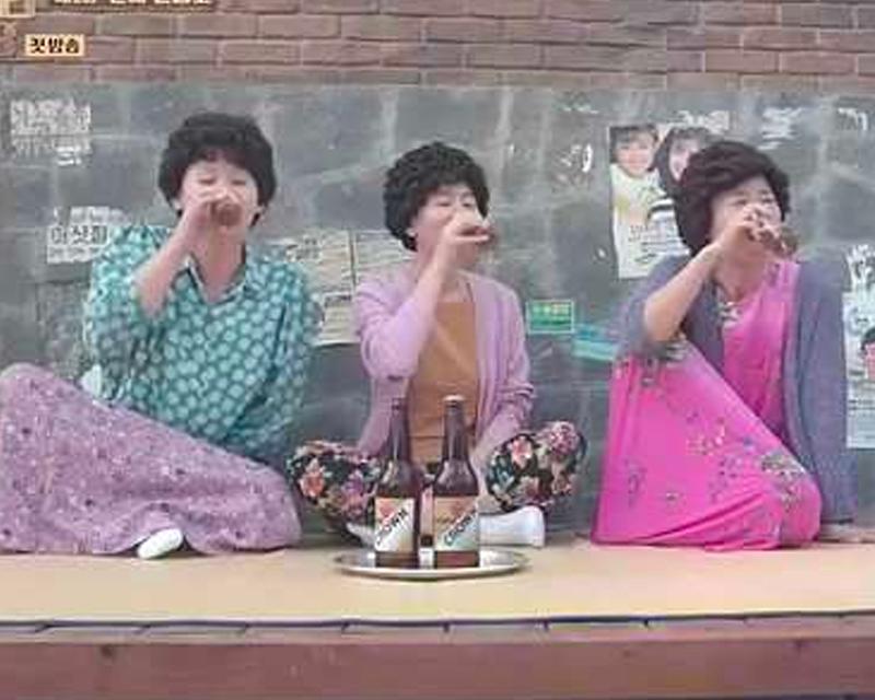 三位中年婦女坐在户外平台上的照片，面部模糊，桌上有韓國啤酒