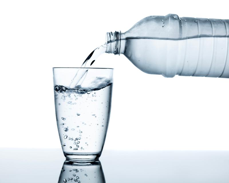 將瓶裝水倒入玻璃杯中的照片