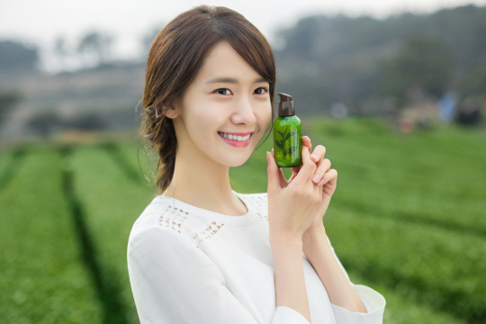 潤娥手持Innisfree綠茶精華瓶，站在綠茶田中，展現品牌天然成分。