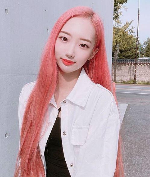 ピンクの髪とスタイリッシュな白いジャケットを着用している女性の全身写真。彼女はセクシーかつカジュアルなファッションを披露している。