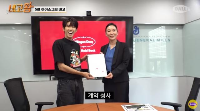 ファン・グァンヒがハーゲンダッツとの契約書を持っている姿。背景にはハーゲンダッツのロゴがディスプレイに映っている。