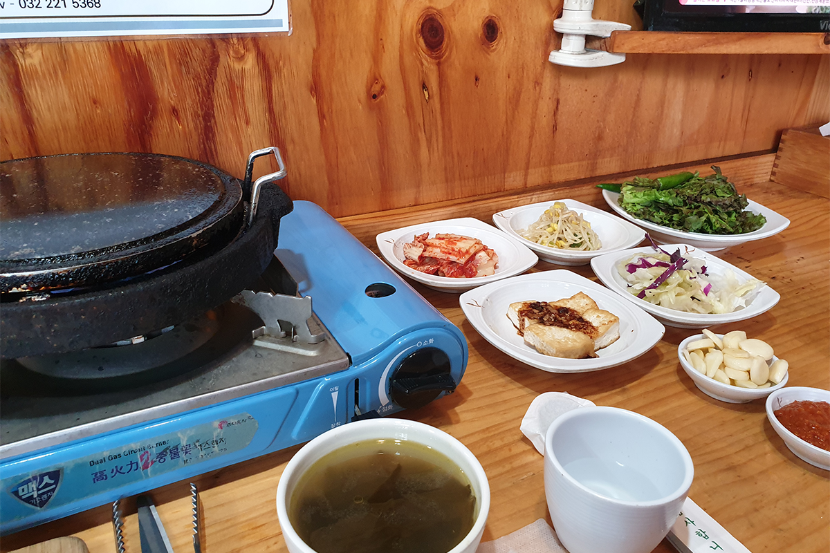 韓國富川獨孤真1人食堂的單人燒肉座位設置，展示了小型煤氣爐和各類韓式小菜，包括泡菜和豆芽等，創造出温馨的單人用餐體驗。