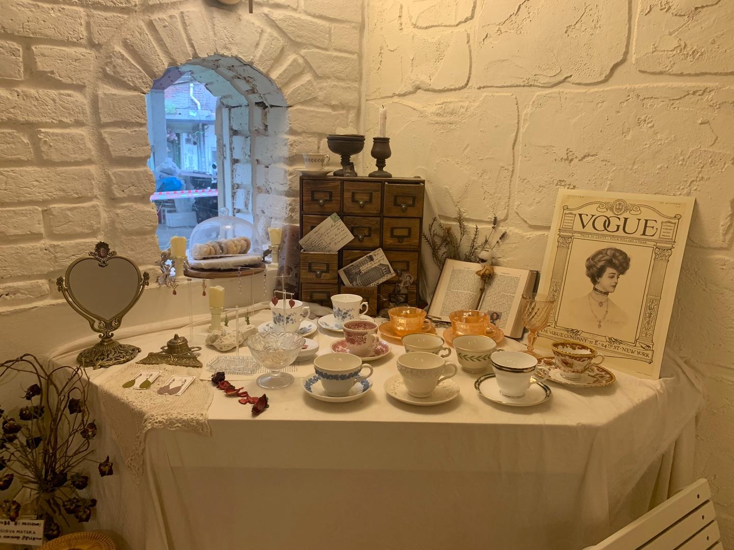 アンティーク風のインテリアで装飾されたカフェの一角。色とりどりのティーカップとミラー、小物が並んでいて、温かみのある雰囲気が漂います。