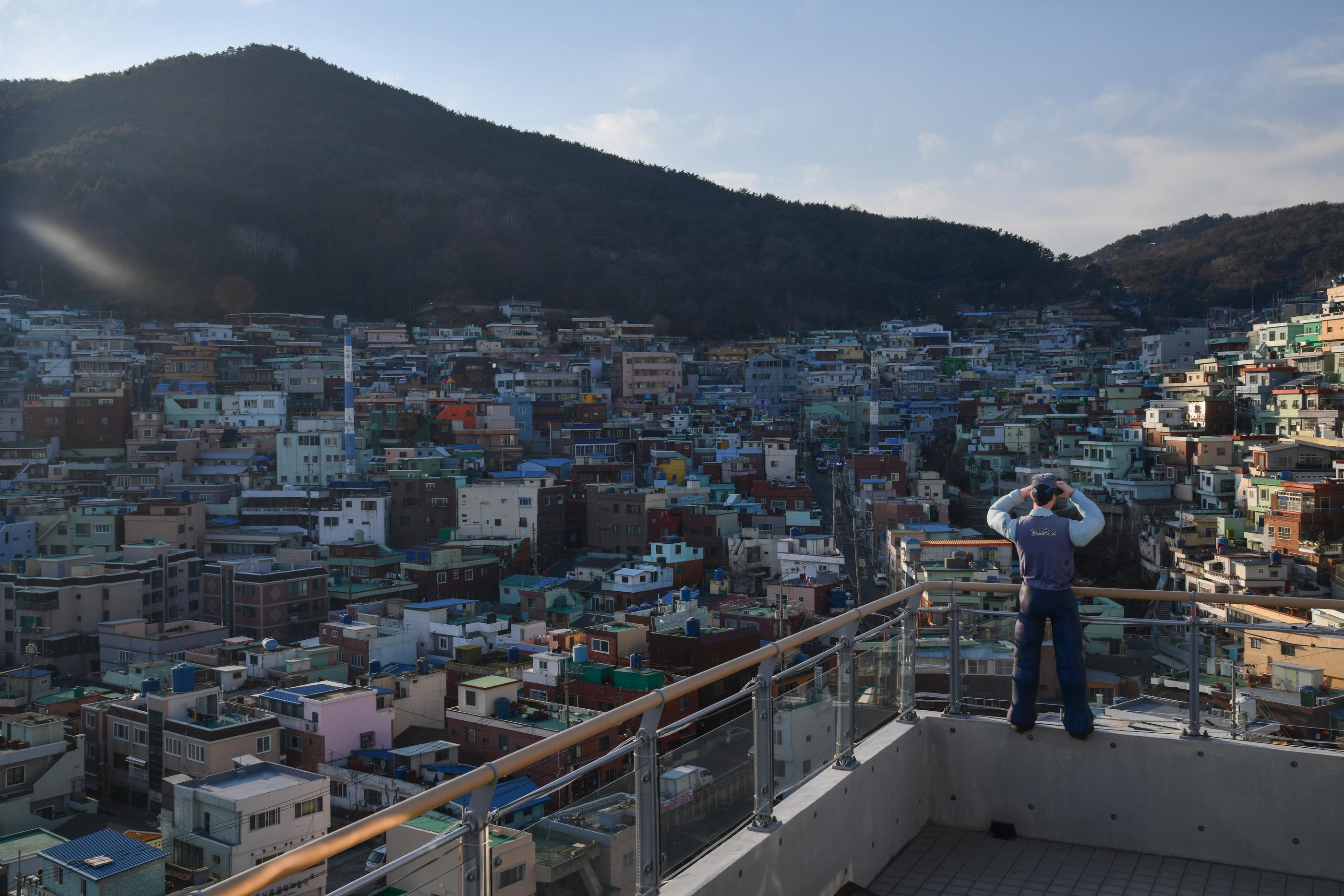 釜山のホチョンマウル遠景。色彩豊かな密集した住宅街と、背景にそびえる山が映し出されています。