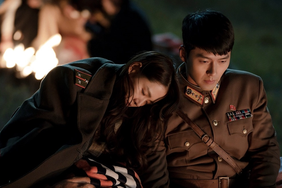 穿著軍裝的兩人在夜晚篝火前共享親密時光。《愛的迫降》以其跨越國界的愛情故事，成為韓劇中的經典代表。