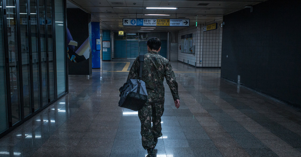 一名身穿迷彩服的韓國大學生在地鐵站內前行，準備去當兵