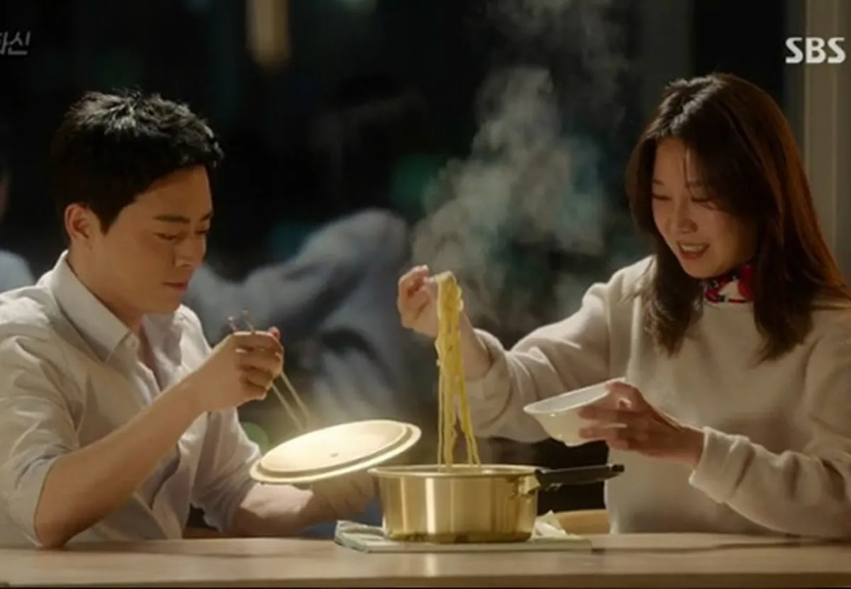 สองคนกำลังนั่งรับประทานราเมนในซีรี่ส์เกาหลี โดยราเมนถูกเสิร์ฟในหม้อสีทองที่มักใช้ในบ้านเกาหลี