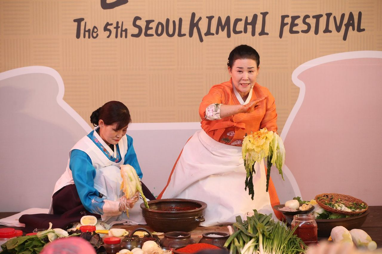 two ladies wearing hanboks showcasing their cabbage kimchi at a festival