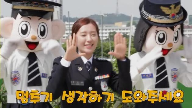 韓国警察の制服を着た女性とマスコットキャラクターが、歌に合わせてジェスチャーをしている様子が映されています。