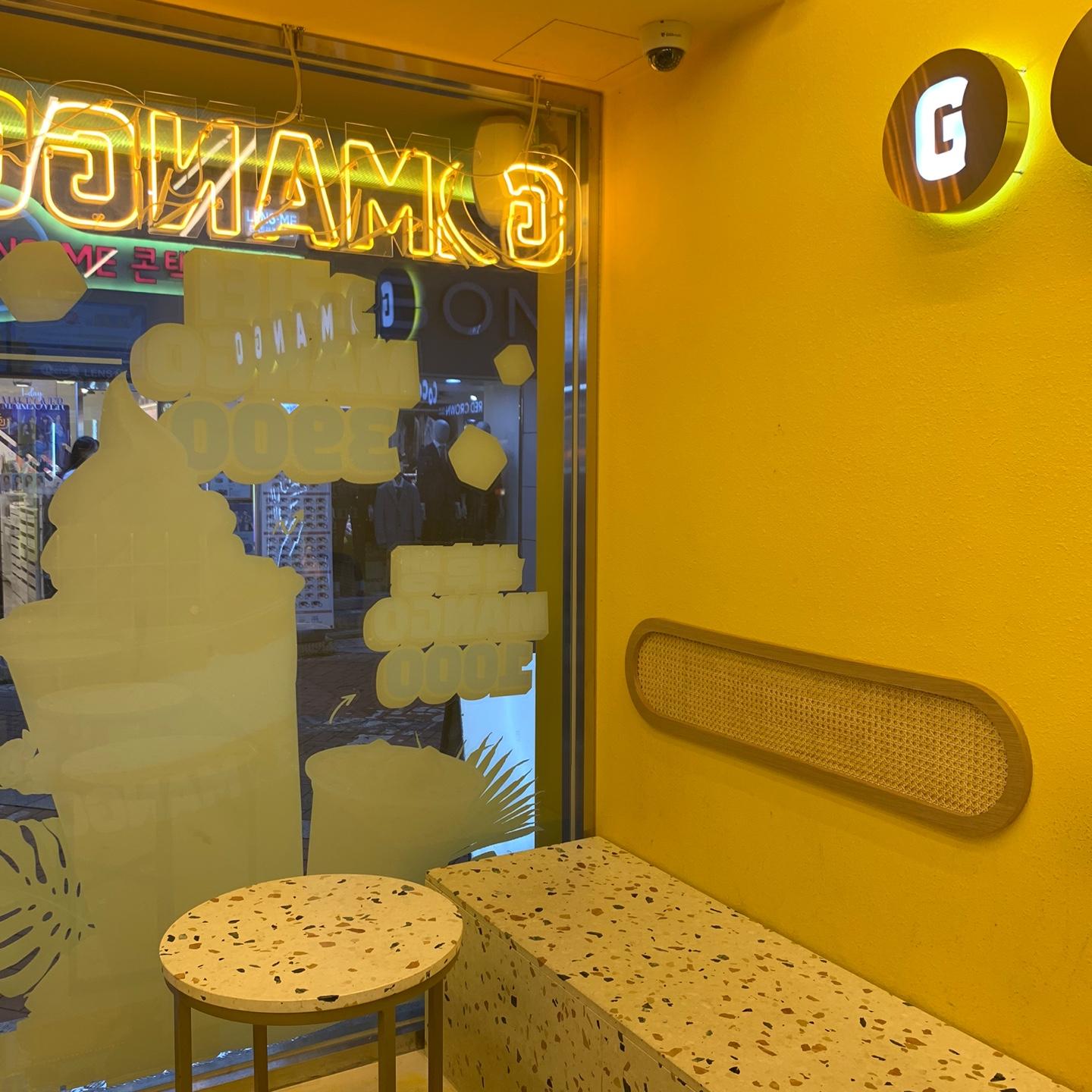 GO MANGO 카페의 노란 내부와 벽에 장식된 네온사인. 카페의 좌석과 인테리어 모습.