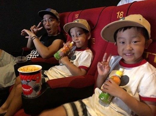 一家四口坐在電影劇院內，享受著親子的樂趣，一起拿著飲料和爆米花。