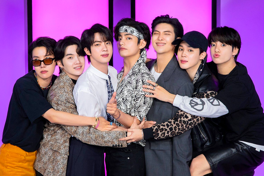 BTS偶像團體成員以團結姿勢擁抱在一起，背景為粉紅色光影，展示出他們的友情和影響力。