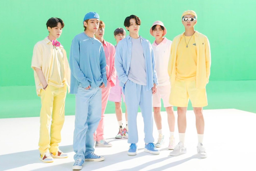韓國男子偶像團體BTS身穿色彩繽紛的服裝，站在綠色背景的戶外，展現韓流流行文化的獨特魅力。