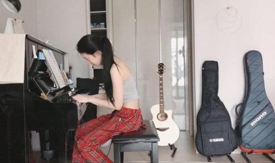 チャン・ジェイン、ピアノの前に座っている室内の写真、背景にギターのケースが見える