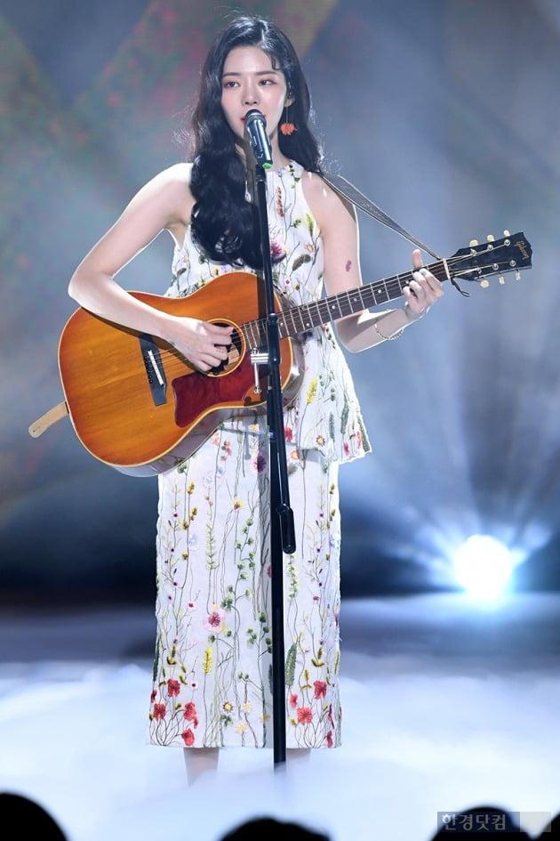 ステージでギターを弾くチャン・ジェイン、花柄のドレスを着ている