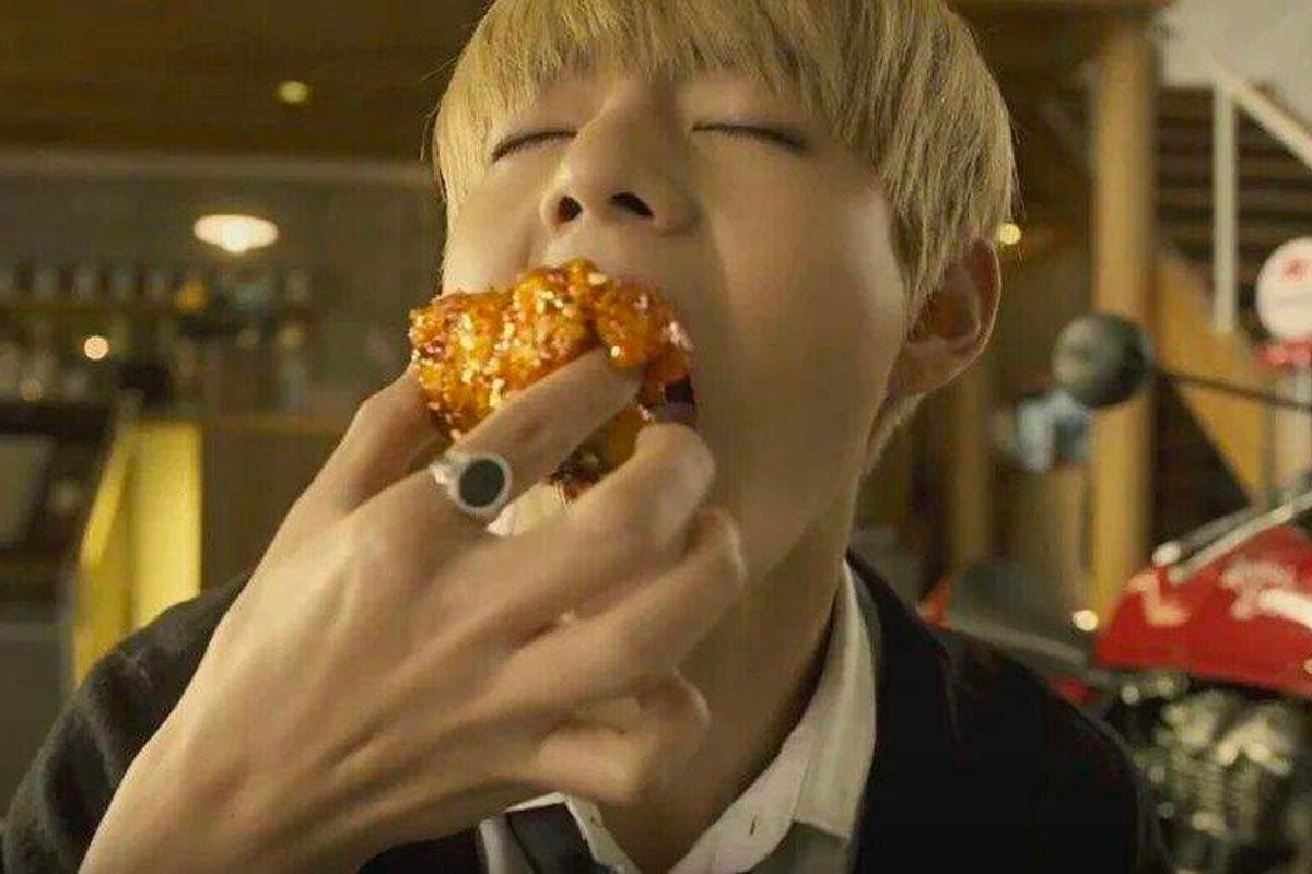 韓國炸雞店內,一名顧客正在使用手持炸雞,背景可見紅色摩托車。