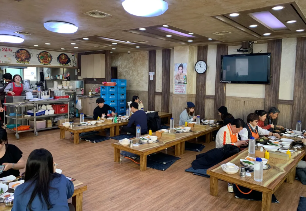 韓国の伝統的な食堂で低いテーブルで食事をする人々。韓国で一般的な座って食事をするスタイルを反映した風景。