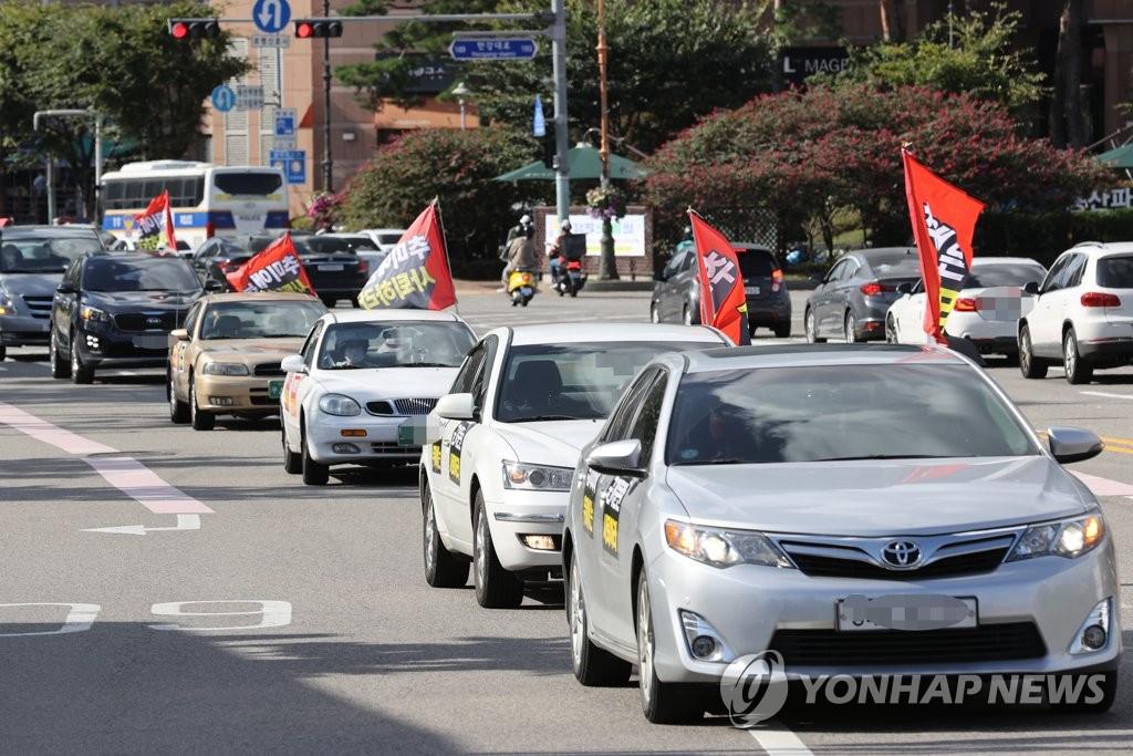ขบวนรถที่กำลังเคลื่อนผ่านถนนในเกาหลีใต้ในช่วงการประท้วงแบบ Drive-thru โดยมีธงสีแดงติดอยู่บนหลังคาเพื่อแสดงสัญลักษณ์ในการประท้วงรัฐบาล